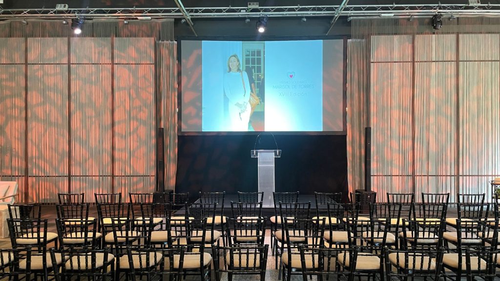 Montaje de sala con sillas Tiffany, escenario con atril y gran pantalla de proyección central para el evento de la XVIII edición del premio solidario Marisol de Torres en la Quinta de Jarama
