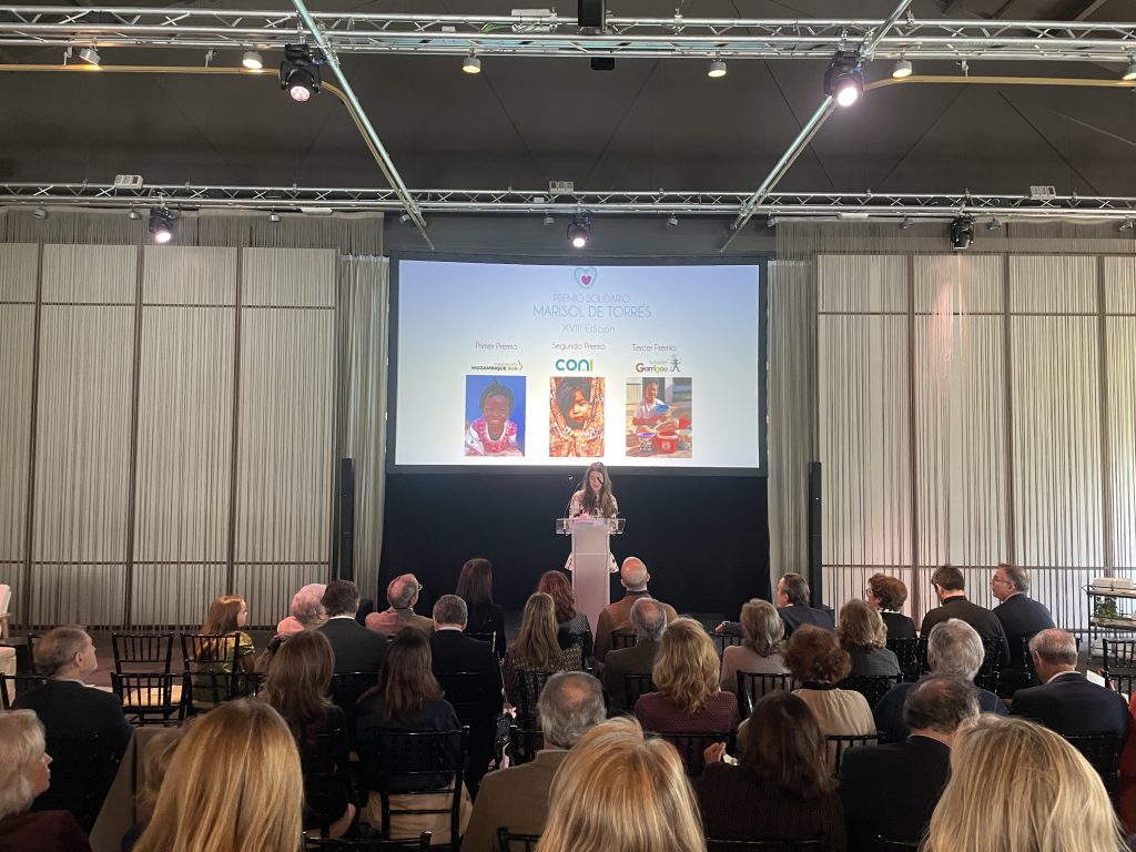 Mujer hablando desde el escenario y público escuchando en el evento de la XVIII edición del premio solidario Marisol de Torres en la Quinta de Jarama