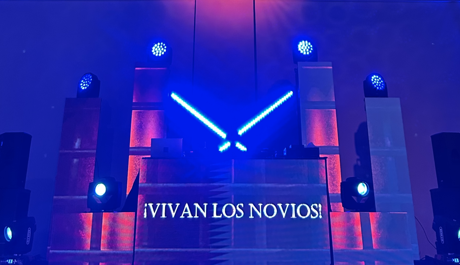 Montaje de iluminación y cabina de DJ con el mensaje '¡VIVAN LOS NOVIOS!' proyectado en una celebración de boda en La Quinta de Jarama.
