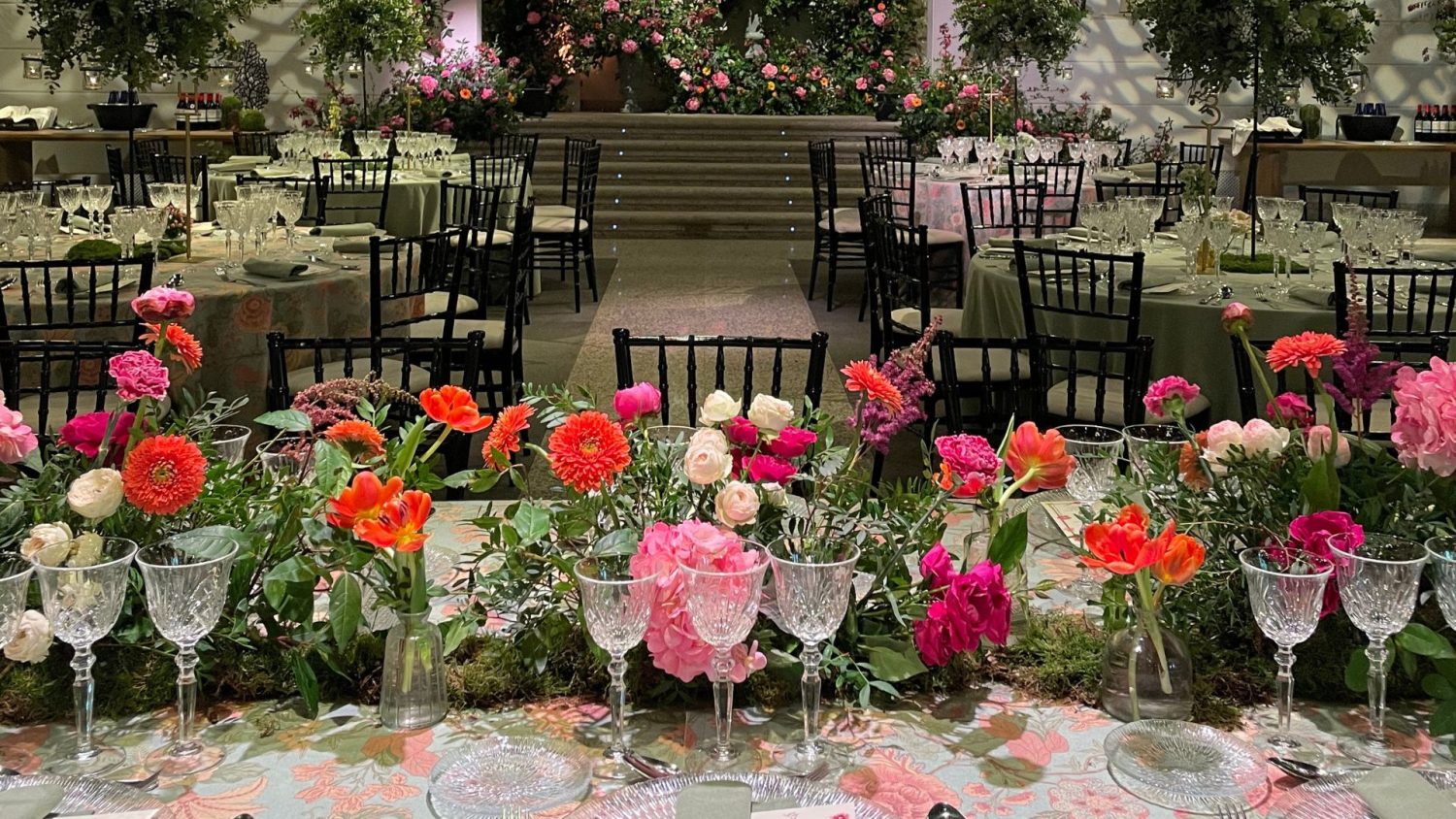 Salón de banquetes con mesas vestidas con mantelería floral y centros de mesa en color rosa y espectaculares centros de mesa elevados con vegetación en la Quinta de Jarama.