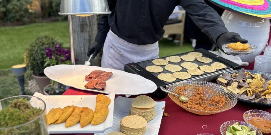 Vista detallada de un chef sirviendo un plato mexicano recién hecho con guarniciones en un plato pequeño, parte de una experiencia de cocina en vivo dinámica para invitados en una boda al aire libre en La Quinta de Jarama.